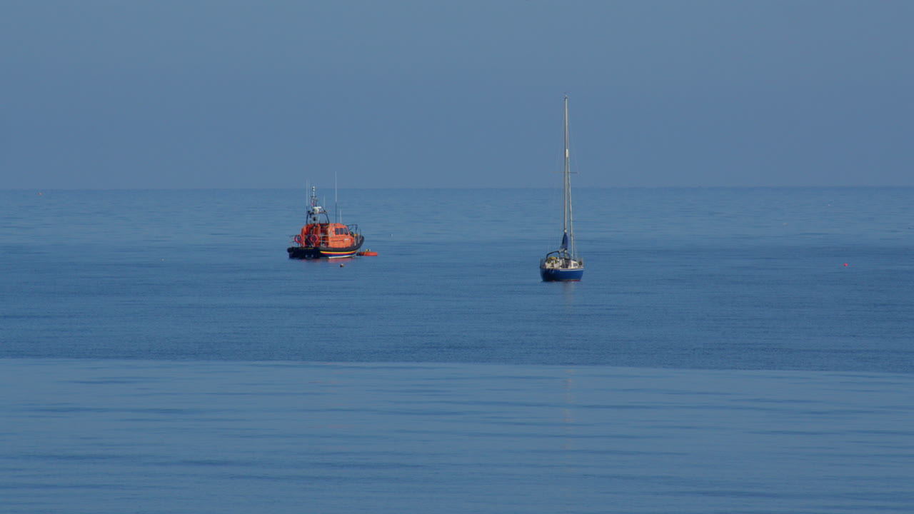 Wide shot of lifeboat and sailboat moored at sea at new quay bay