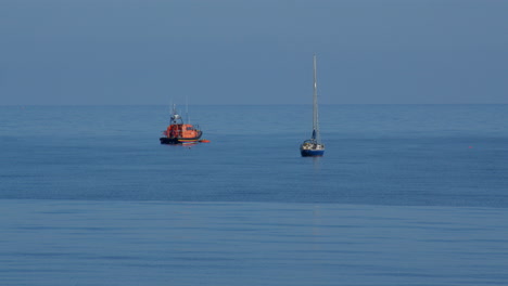 Wide shot of lifeboat and sailboat moored at sea at new quay bay