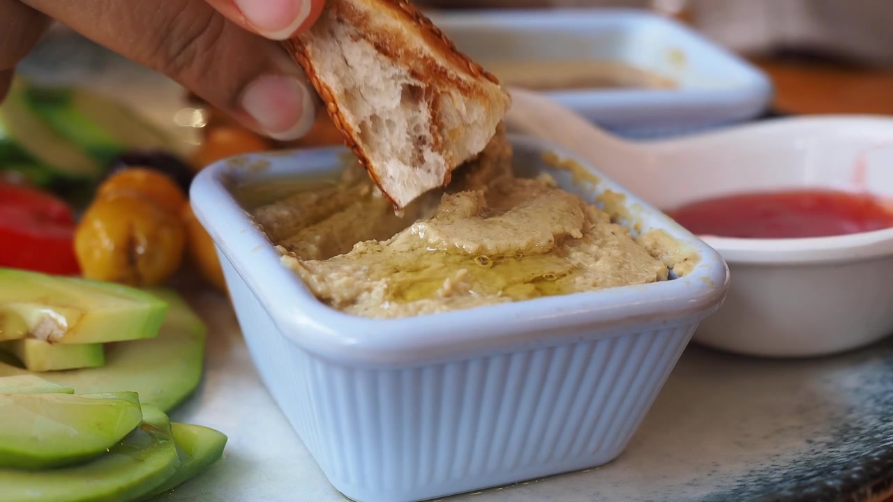 Primo piano di una mano che intinge pane al sesamo nell'hummus