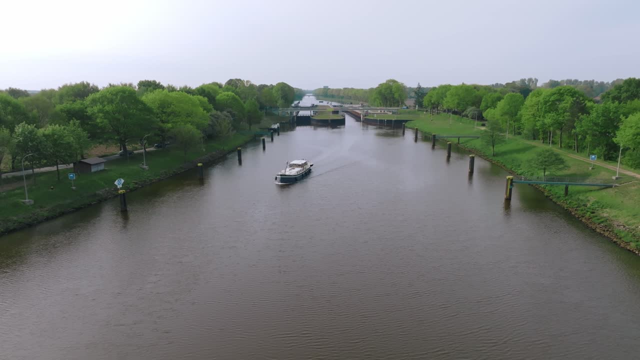 Zoom in aerial shot of a barge approaching Doerpen Lock on the Küstenkanal. Clear weather and farmland patterns define the rural landscape.
