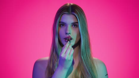 medium slow motion shot of a young attractive blonde woman while applying red lipstick on her lips to get ready for the evening or date while looking sexy to the camera in front of purple background