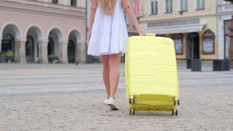 vertical video woman walking on the cobblestones against the background of the city, pulling a yellow suitcase. tourist woman travels. baggage. yellow suitcase