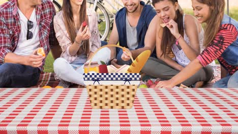 animation of picnic basket on gingham tablecloth and happy diverse friends having picnic in park