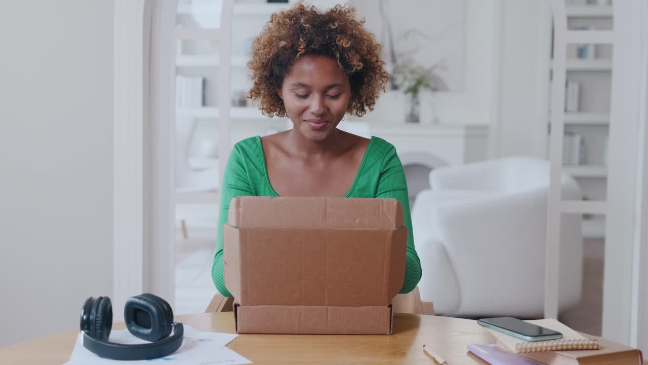 Young smiling african american woman unpacks box from online store sits at table