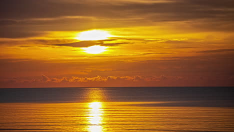 The-golden-sun-reflects-off-the-surface-of-the-ocean-as-clouds-cross-the-sky-blowing-in-different-directions-at-sunrise---time-lapse