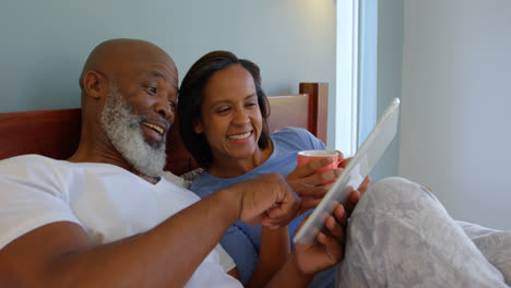 Front-view-of-mature-Caucasian-couple-using-digital-tablet-on-bed-in-a-comfortable-home-4k