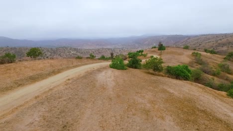 cyclist on a dirt road with mountain bike riding downhill very fast in beautiful landscape hills of equador - drone shot