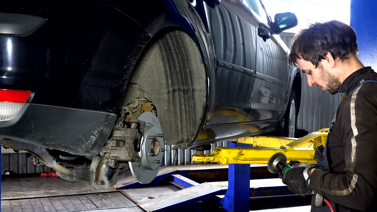 hombre mecánico moliendo pernos oxidados con una herramienta de molienda eléctrica cerca de un coche levantado