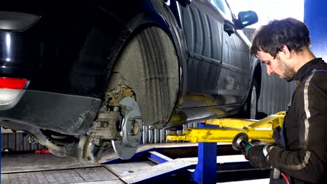 hombre mecánico moliendo pernos oxidados con una herramienta de molienda eléctrica cerca de un coche levantado
