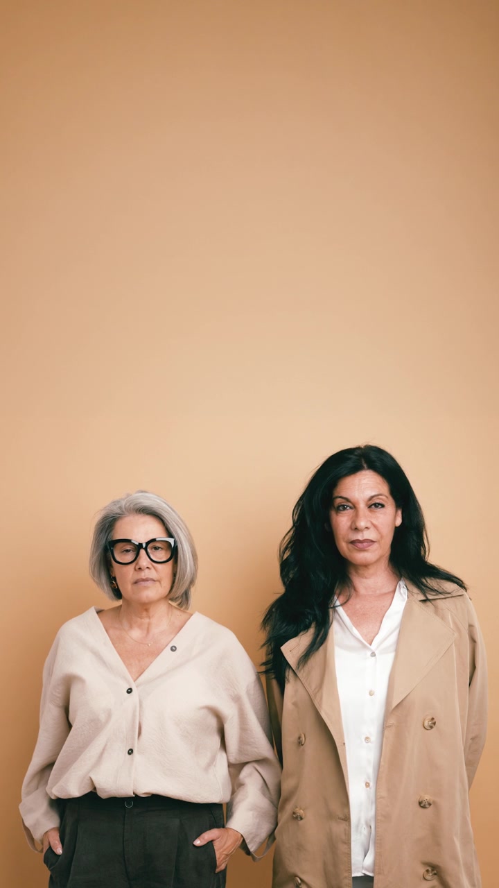 Two Mature Women Standing Together Against a Neutral Background
