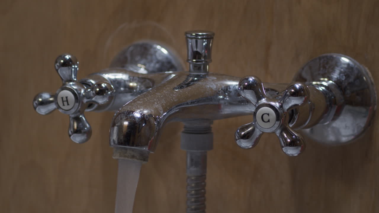 la mano gira la manija de agua caliente para abrir el grifo de agua del baño