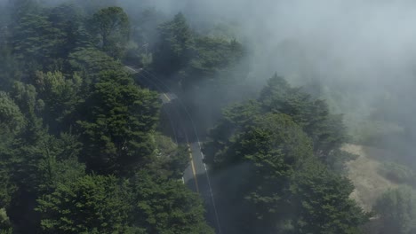 구부러진 산길 위로 공중 드론이 발사되고, 몇 대의 자동차가 지나가고, 드론은 저수지와 고속도로를 배경으로 드러내기 위해 기울어져 안개 낀 숲 위로 앞으로 이동합니다.