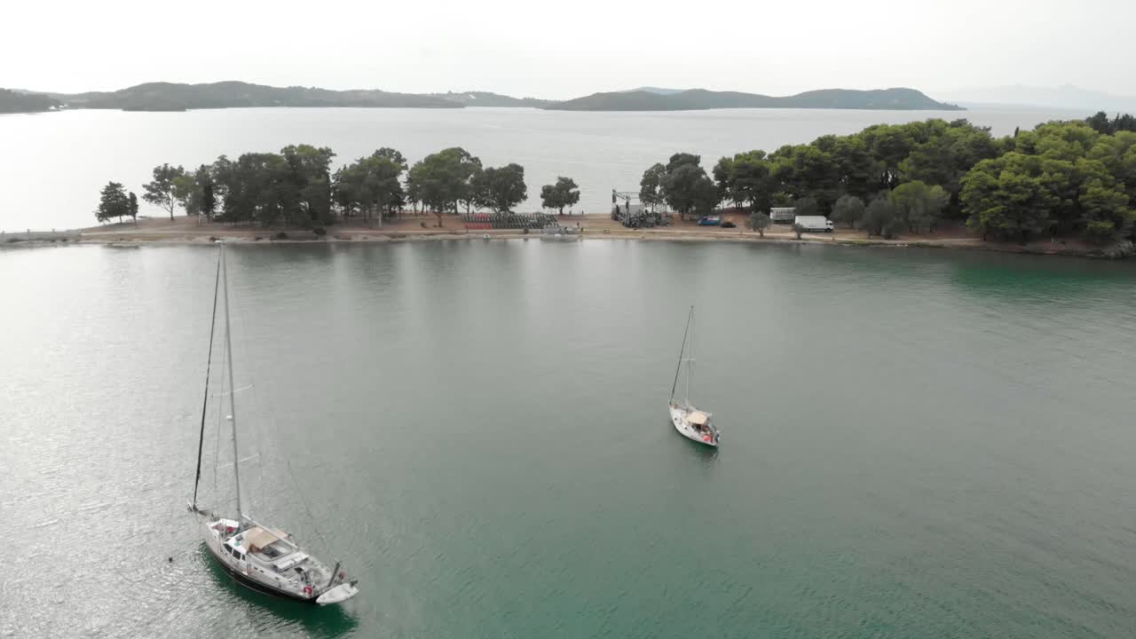 Ripresa aerea con drone di yacht che navigano in un mare turchese, barche a vela, incredibile stile di vita lussuoso, esotico e panoramico con montagne verdi sullo sfondo e la piccola isola greca di Kukumitsa, bellissimo paesaggio