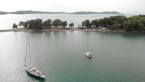 aerial drone shot of yachts sailing in turquoise sea ,  sailboats, amazing exotic scenic luxury life style  explore green mountains at background and kukumitsa  greek small island, beautiful landscape