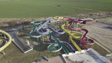 toma aérea hacia atrás del parque acuático cerrado durante el día soleado rodeado de campos rurales