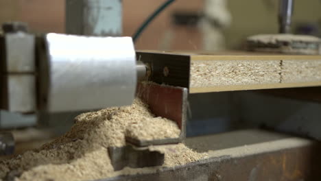 horizontal technical drill bit goes in and out into chipboard wooden element, producing a lot of flying sawdust arround