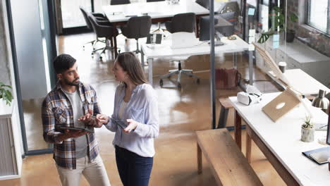 Young-Caucasian-woman-and-Asian-man-discuss-business-over-a-tablet-in-an-office