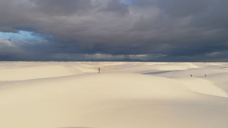 4k-Antenne-Eines-Mannes,-Der-Auf-Einer-Weißen-Sanddüne-Steht,-Mit-Herannahendem-Sturm-In-Der-Ferne