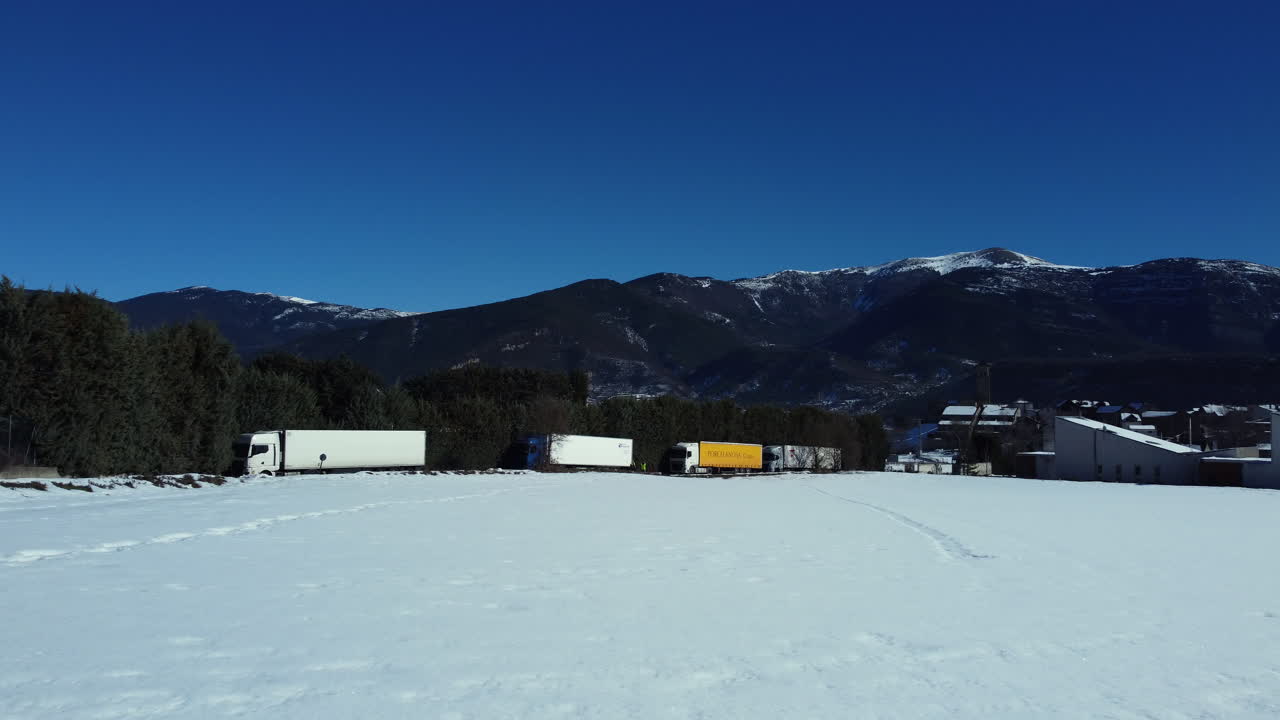 Trucks parked in a snowy field with mountains in the background