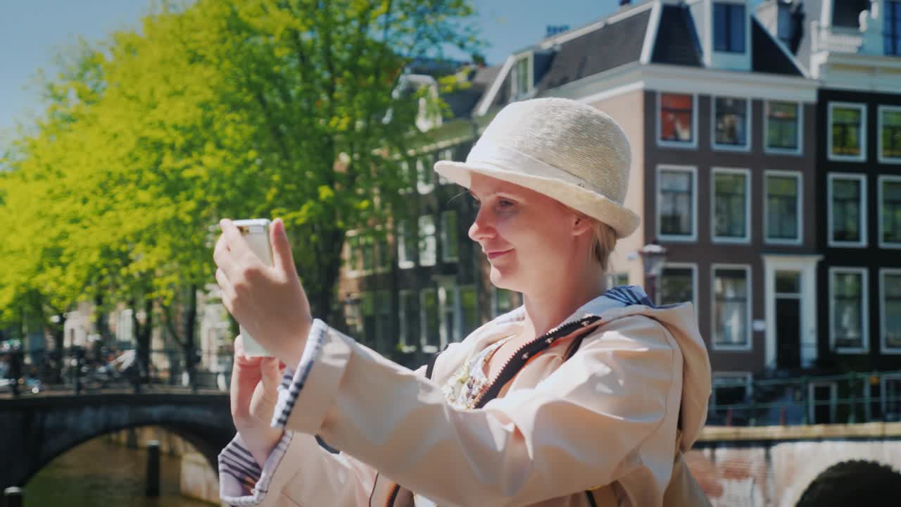 A woman tourist takes pictures of herself in a picturesque place near the canal. Tourism in the Netherlands and Amsterdam