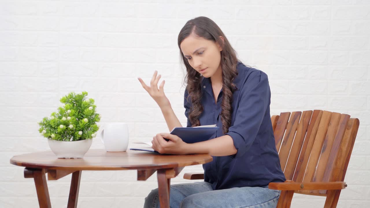 chica india conmocionada leyendo un libro en una cafetería
