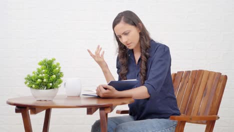 chica india conmocionada leyendo un libro en una cafetería