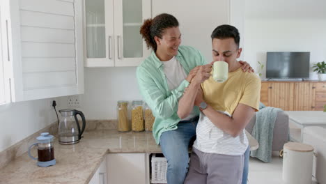 happy diverse gay male couple having coffee and embracing in kitchen, copy space, slow motion