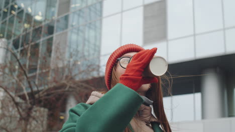 Woman drinking coffee outside a modern building in winter