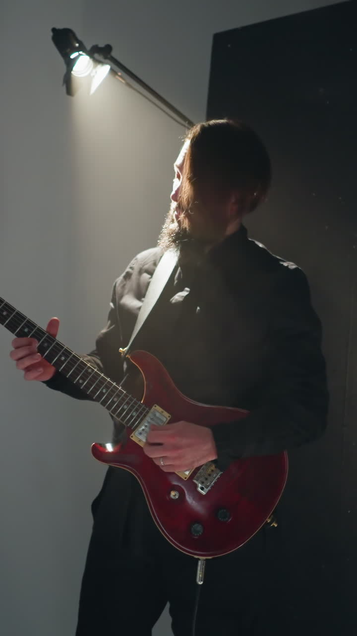 Dynamic shot of a guitarist in black playing a red electric guitar against a plain white background with active camera zooming
