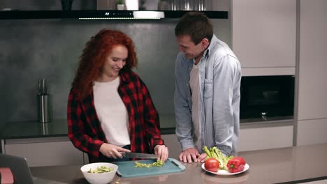 Una-Pareja-Divertida-Mientras-Cocinan-Juntos-En-Una-Cocina-De-Color-Gris,-Una-Familia-Joven-Y-Activa-Que-Se-Divierte-Riendo-Se-Siente-Despreocupada.-Un-Hombre-Feliz-Vino-A-La-Cocina-Después-Del-Trabajo-En-Busca-De-Ayuda,-Disfruta-De-La-Preparación-De-La-Comida