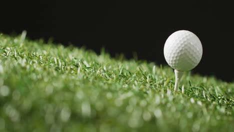 close up of golf tee and ball on grass and black background, copy space, slow motion