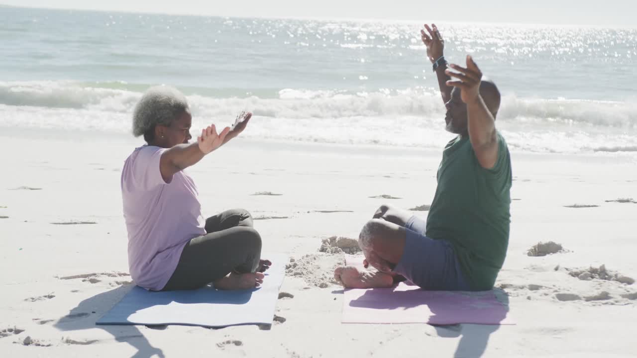 una feliz pareja afroamericana haciendo yoga y meditando en la playa, en cámara lenta