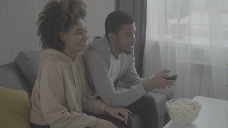 una joven pareja afroamericana escogiendo una película con el mando a distancia.