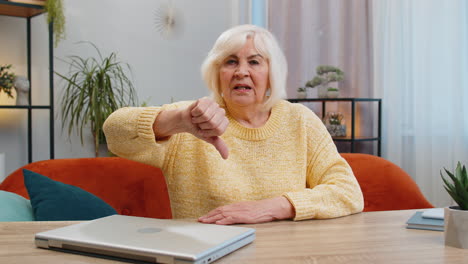 upset senior woman showing thumbs down, dislike bad work, disapproval, dissatisfied feedback at home