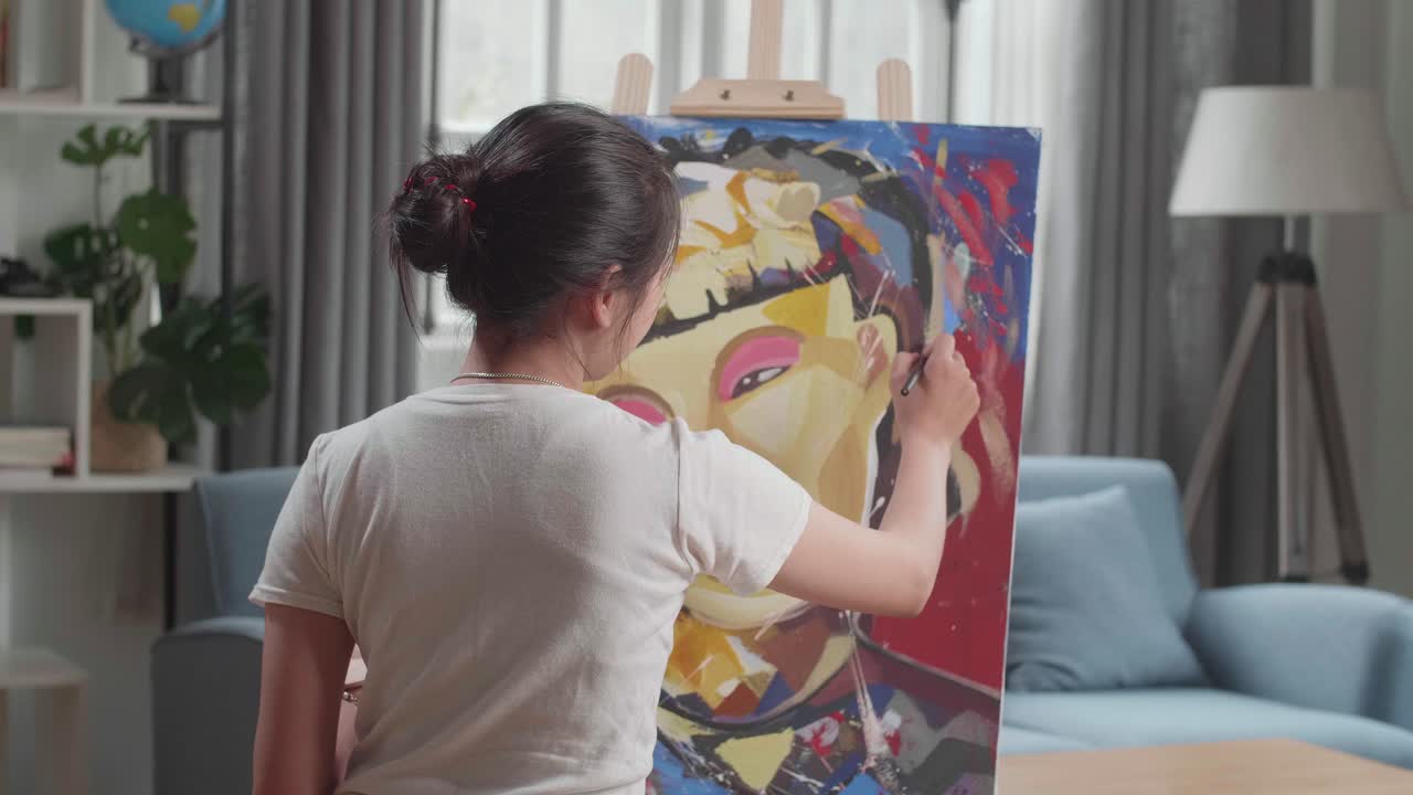 Hind View Of An Asian Artist Girl Holding Paintbrush Mixed Colour And Painting A Girl'S Face On The Canvas