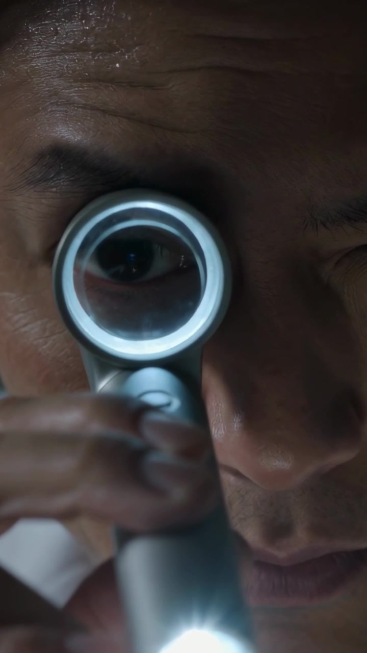 Vertical video: Moving Asian man tapping loupe button, boosting LED and enlarging right eye at exam