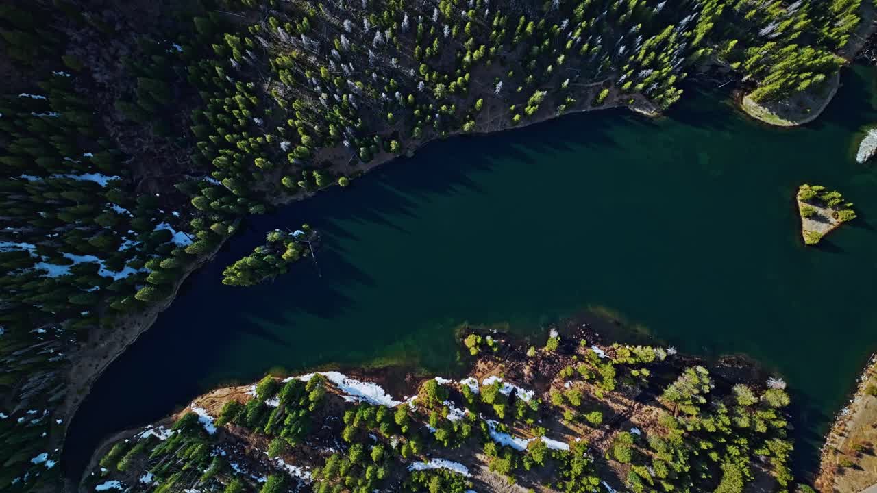 Curved lake bends through Frisco Gulch’s lush green pines in late afternoon light, top shot drone descend