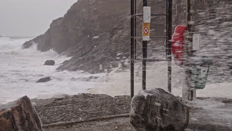 nieve soplada por un fuerte viento con olas rompiendo en las rocas