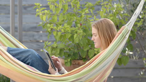 using tablet, woman relaxing in hammock in backyard garden