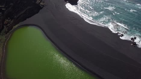 aerial of green lagoon in lanzarote island secluded remote isolated black sand lava beach in los volcanes national park