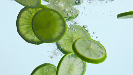 la cal cortada en rodajas tropicales dejó caer agua en el fondo blanco de primer plano. salpicaduras de cítricos