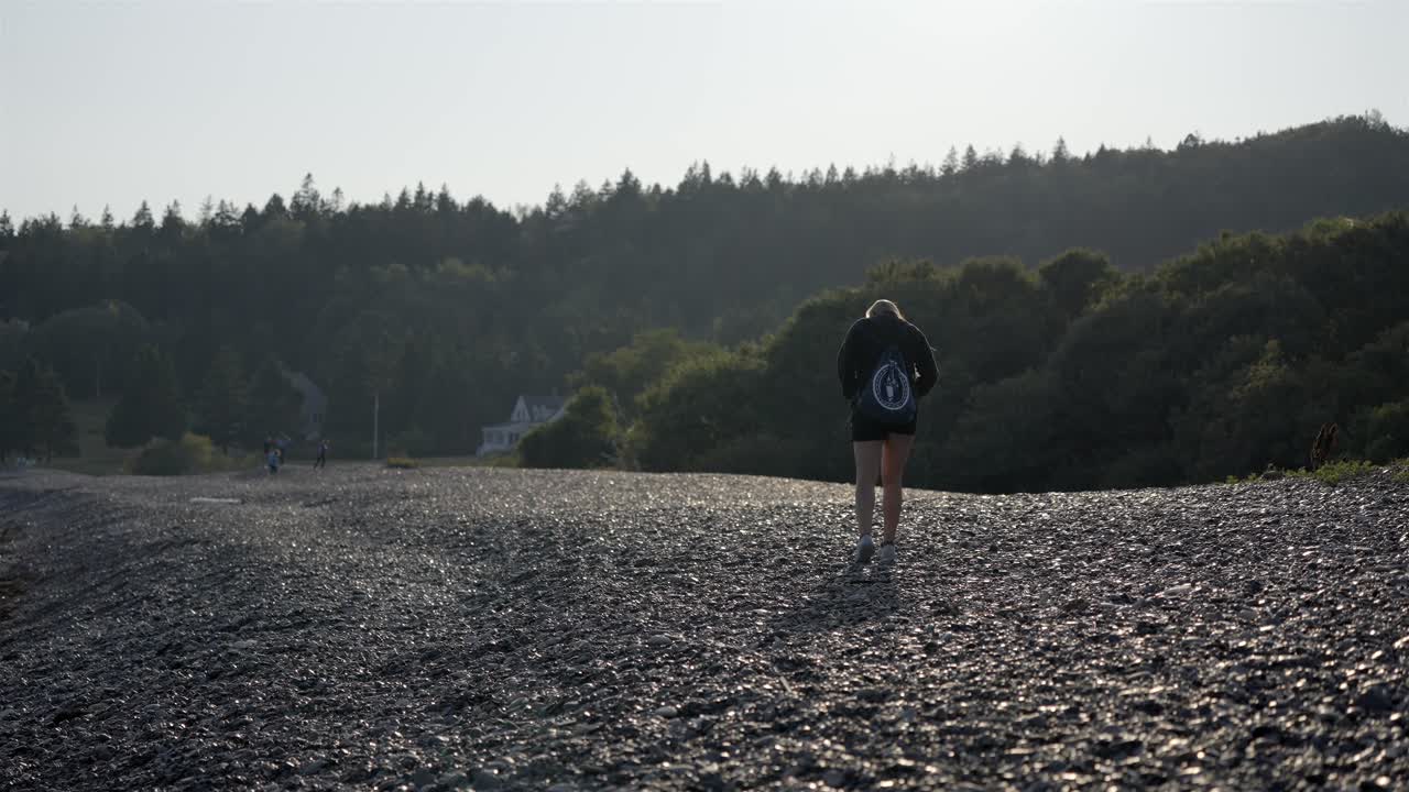 Woman with a backpack enjoys a solitary walk on the rocky Jasper Beach