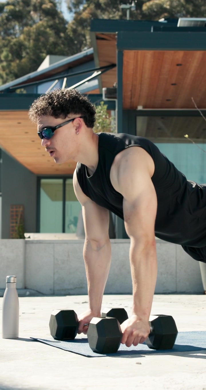Young Man Doing Push-Ups with Dumbbells Outdoors