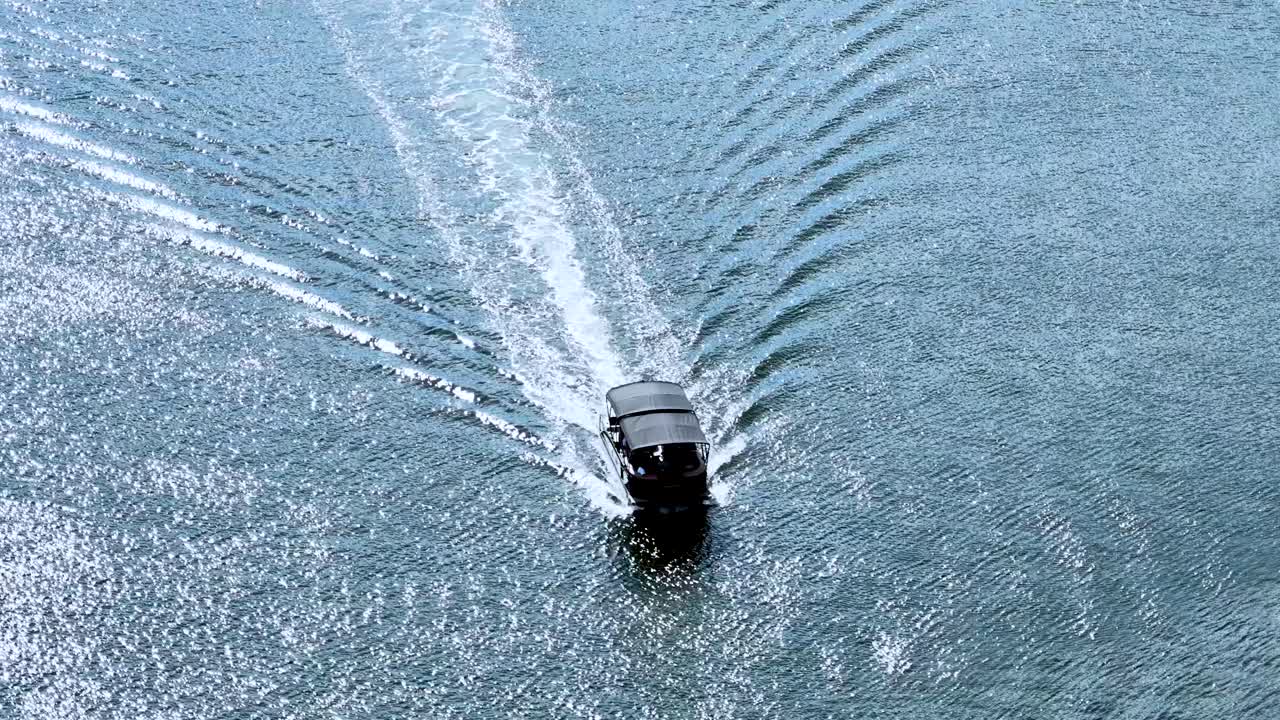 A speedboat moves swiftly across sparkling water, aerial perspective, midday sunlight, calm maritime setting