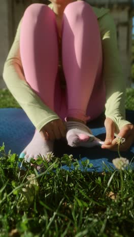 woman wearing pink leggings and colorful socks sitting on a yoga mat in a park