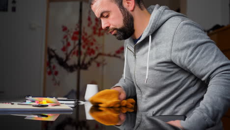 hombre caucásico del este medio limpiando la mesa con superficie de vidrio antes de comenzar a trabajar