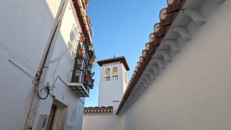 the elegant tower of mezquita mayor de granada rises against a clear blue sky, framed by traditional andalusian architecture and vibrant potted plants. beauty of granada's islamic .