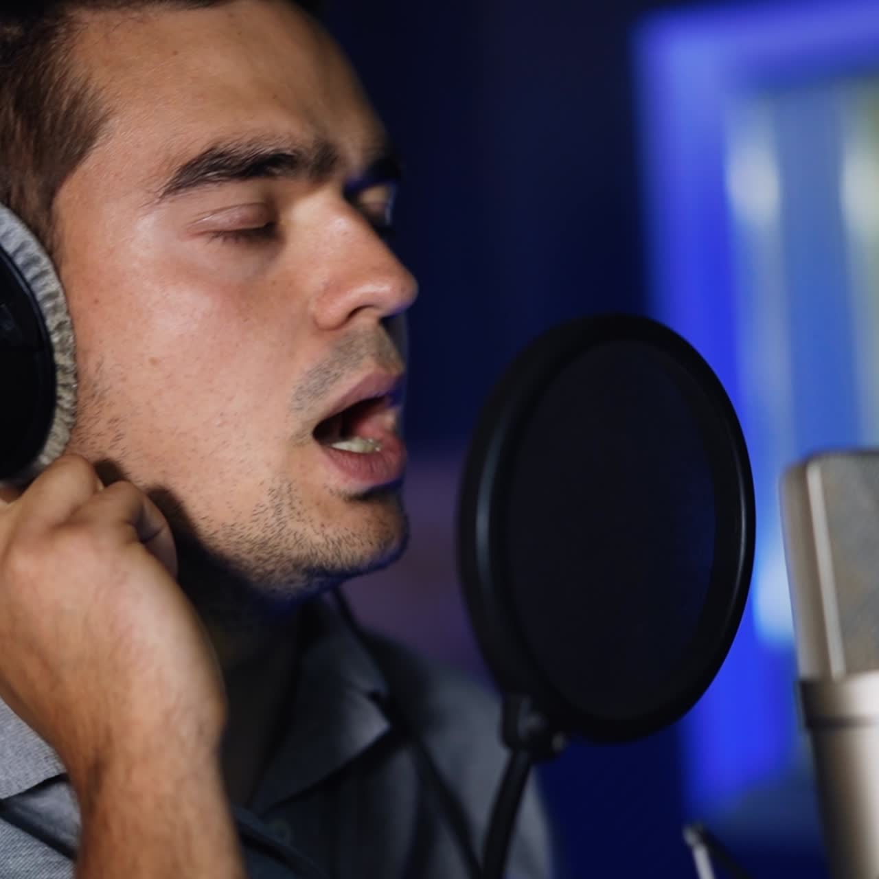 Recording a song in the professional studio. Portrait of a Caucasian male singer in headphones performing song. Close up