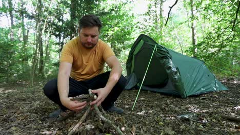 man preparing woods for campfire in front of camping tent in the forest