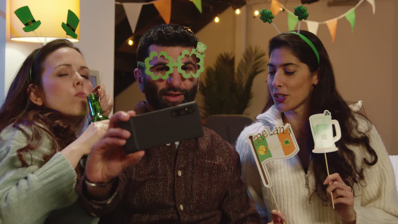 Group Of Friends Dressing Up With Irish Novelties And Props At Home Or In Bar Posing For Selfie Celebrating At St Patrick's Day Party